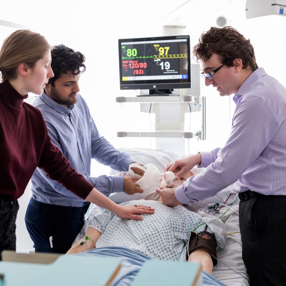 A group of people standing around a patient in a hospital bed.