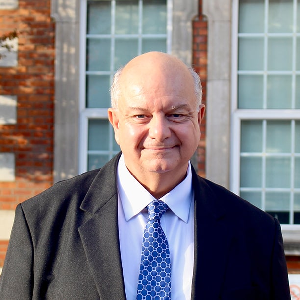 A bald man in a suit and tie standing in front of a brick building.