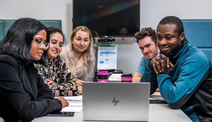A group of people sitting around a table looking at a laptop.